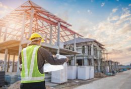 Professional engineer architect worker with protective helmet and blueprints paper at house building construction site background